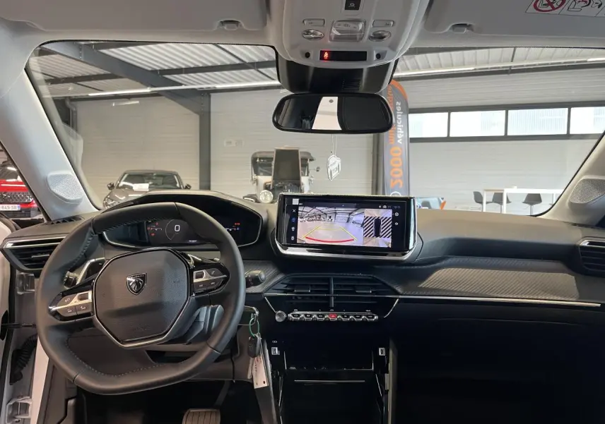 Vue intérieure avant du tableau de bord noir et gris clair de la Peugeot 208 hybride 2025 avec écran tactile et volant compact cuir.