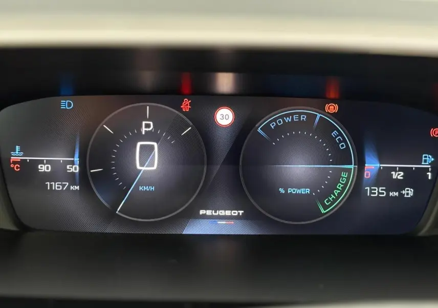 Tableau de bord numérique Peugeot 308 SW Hybrid 2025 affichant vitesse à zéro et indicateurs de charge et température.
