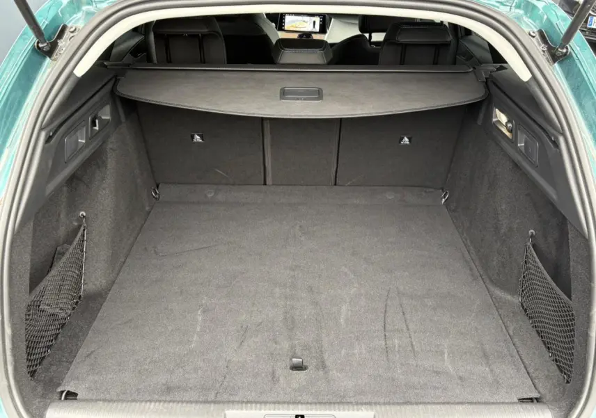 Coffre ouvert vu de l'arrière d'une Peugeot 308 SW Hybrid 145 bleu cuivre, avec filet de rangement latéral et cache-bagages.