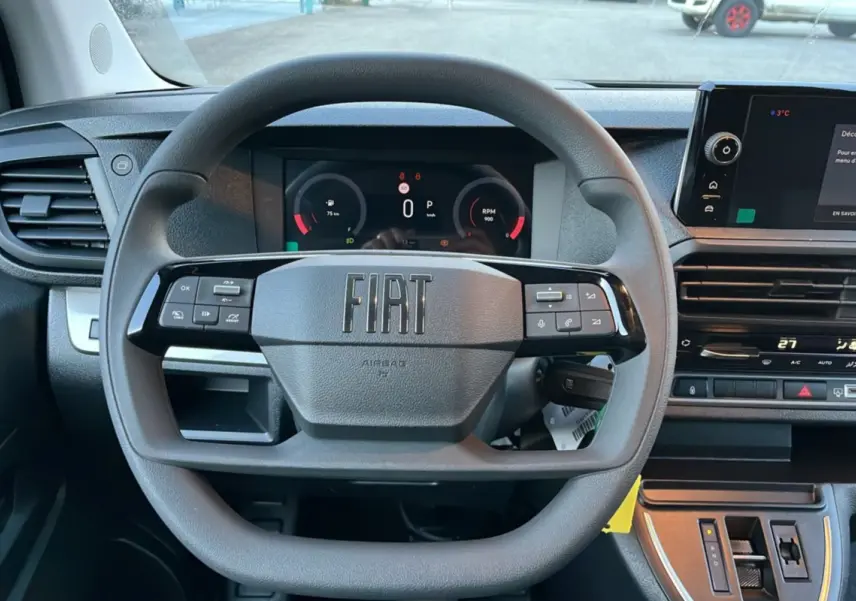 Vue frontale du volant multifonctions noir avec logo FIAT au centre, tableau de bord digital et écran tactile à droite.