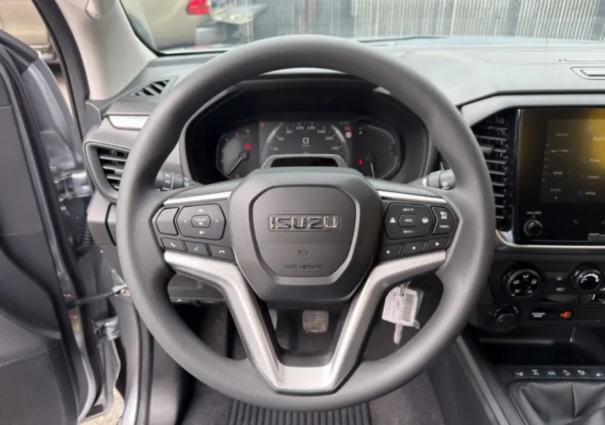Vue intérieure centrée sur le volant multifonctions noir de l'Isuzu D-MAX 2026, avec tableau de bord et écran tactile visibles.