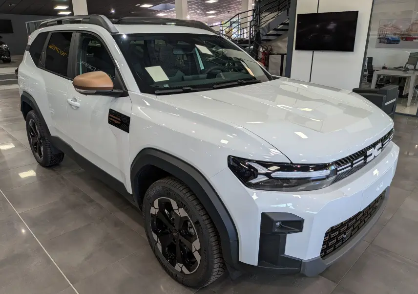 Vue 3/4 avant du Dacia Bigster blanc Glacier avec rétroviseurs bronze et jantes noires en concession.