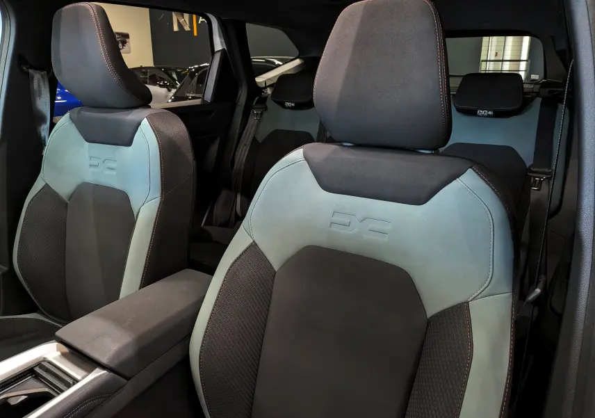 Vue rapprochée des sièges avant bicolores gris clair et noir du Dacia Bigster Hybrid-G 150 4x4, avec logo DS embossé.