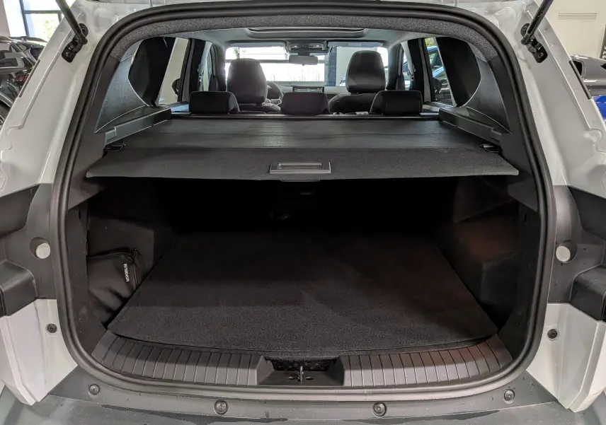 Coffre ouvert vu de l'arrière d'un Dacia Bigster blanc glacier, avec cache-bagages et intérieur noir visible.
