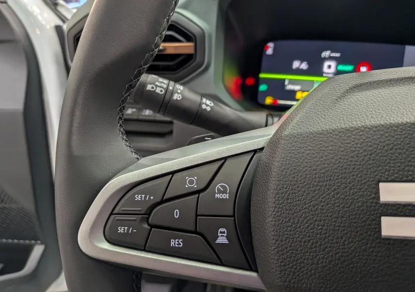 Gros plan sur la partie gauche du volant noir du Dacia Bigster Hybrid-G 150, avec commandes de régulateur et tableau de bord numérique flou.