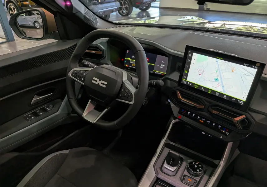 Vue intérieure côté conducteur du Dacia Bigster Hybrid-G 150 4x4 2026, avec écran tactile et volant multifonction noir.