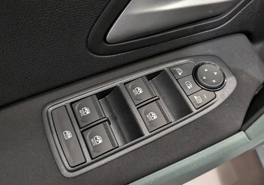 Gros plan sur les commandes de lève-vitres et rétroviseurs électriques sur la porte intérieure noire du Dacia Bigster Hybrid-G 150.