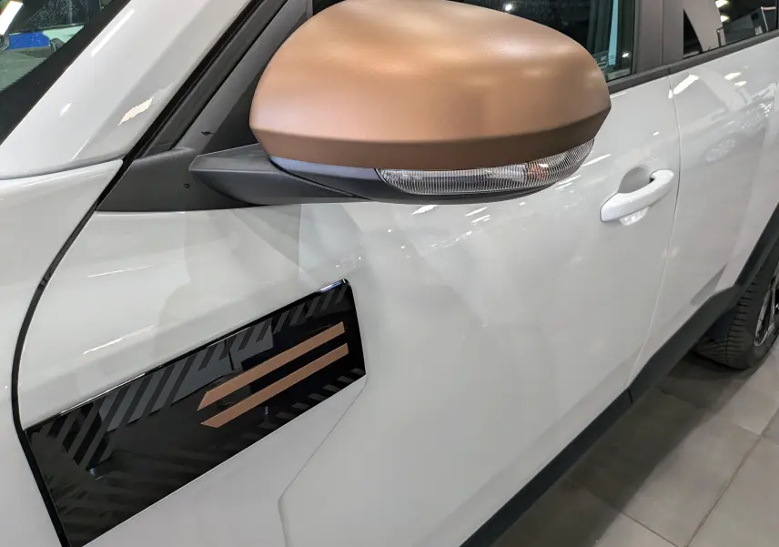 Détail du rétroviseur bronze et de la décoration latérale noire et bronze sur la porte gauche d'un Dacia Bigster blanc Glacier.