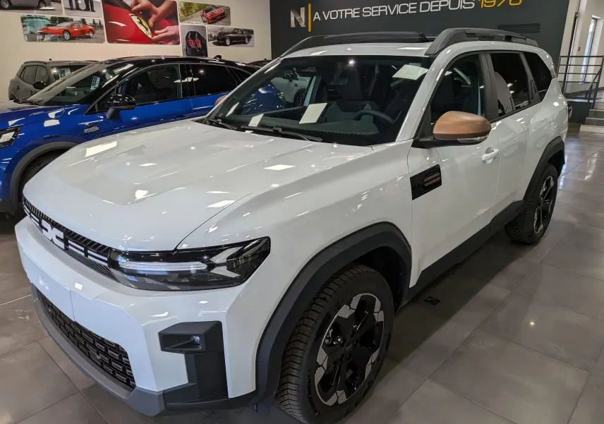 Vue 3/4 avant droite du Dacia Bigster blanc Glacier avec rétroviseurs bronze et jantes biton noir en showroom.