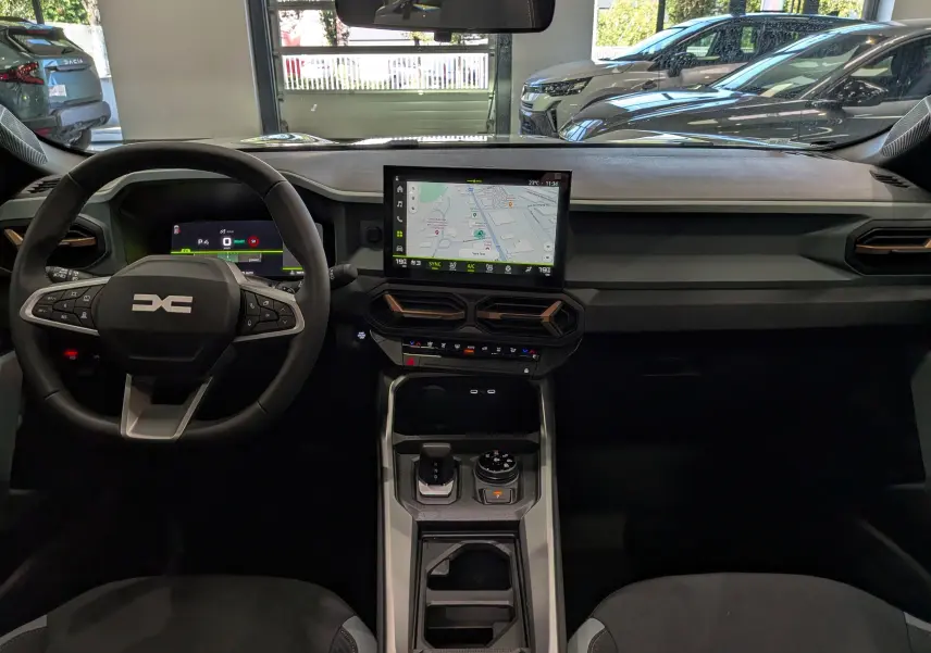 Vue intérieure frontale du tableau de bord du Dacia Bigster Hybrid-G 150 4x4 blanc glacier avec écran tactile central et volant multifonction.