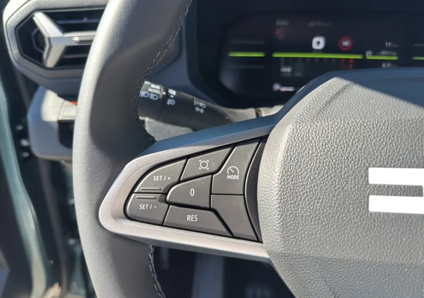 Gros plan sur les commandes au volant côté gauche du Dacia Bigster 2025 vert cèdre, avec affichage numérique en arrière-plan.
