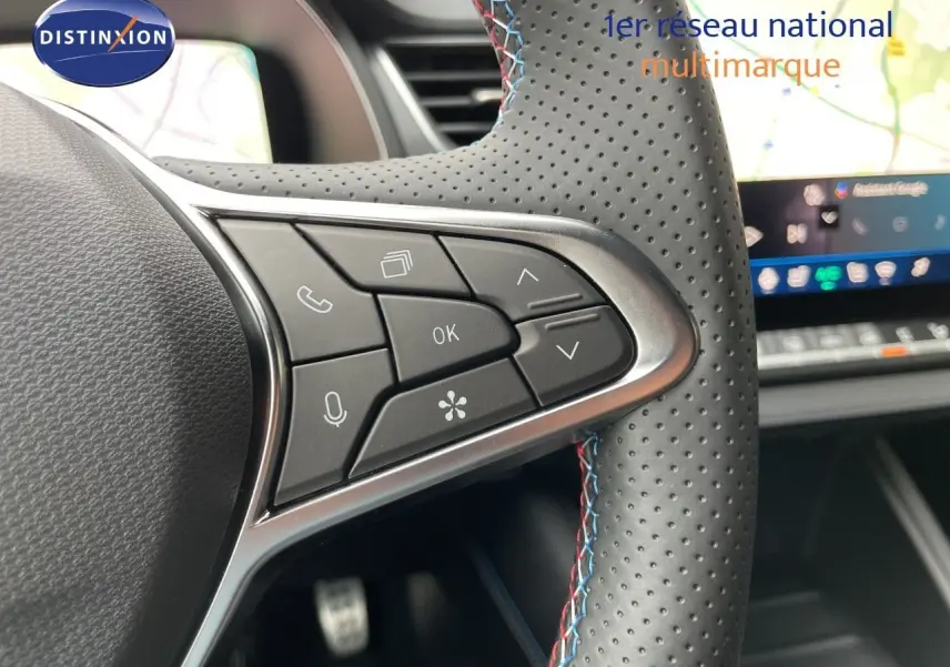 Gros plan sur les commandes multifonctions à droite du volant en cuir perforé avec surpiqûres tricolores, tableau de bord numérique visible.