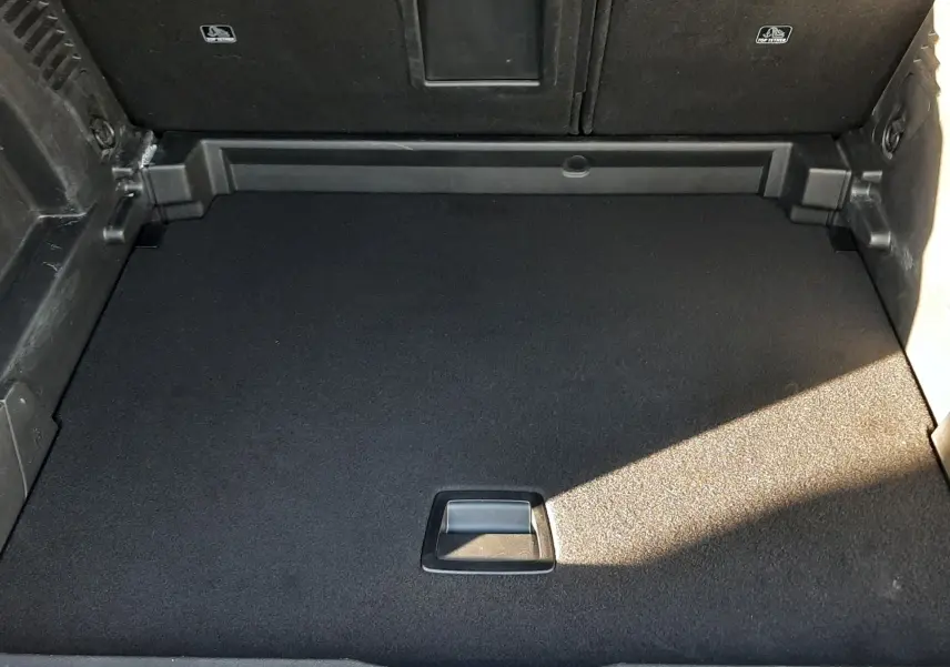 Vue plongeante sur le coffre vide du Peugeot 3008 gris platinium, montrant le tapis de sol et l'accès au rangement sous plancher.