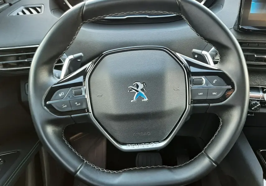 Vue rapprochée du volant noir du Peugeot 3008 2023 avec commandes intégrées et tableau de bord numérique en arrière-plan.