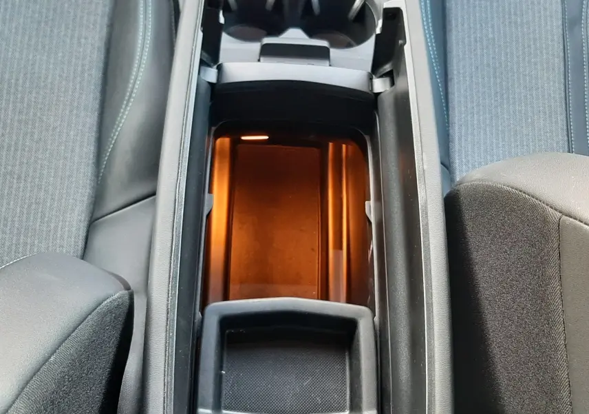 Vue plongeante sur la console centrale ouverte du Peugeot 3008 gris platinium, avec éclairage intérieur orange et porte-gobelets visibles.