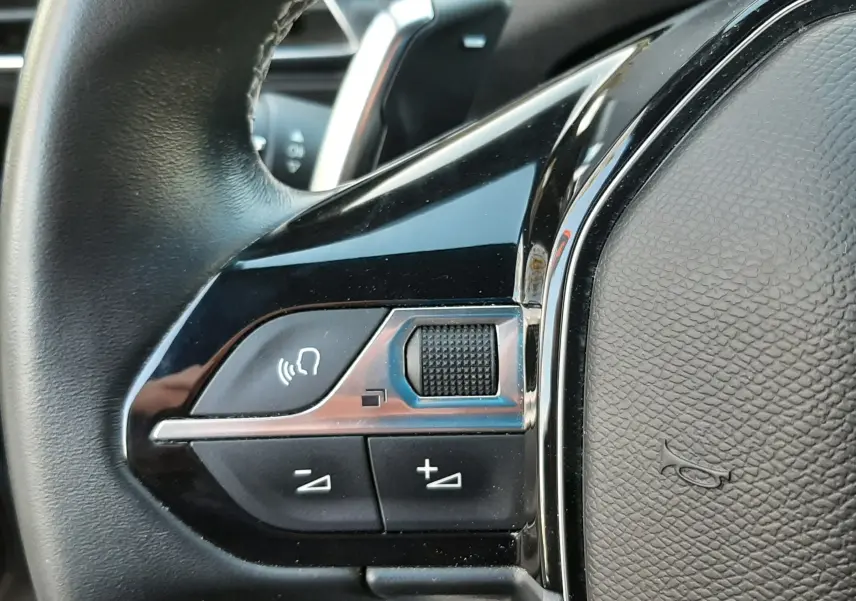 Gros plan sur les commandes gauche du volant en cuir noir du Peugeot 3008 gris platinium, avec boutons de volume et commande vocale.