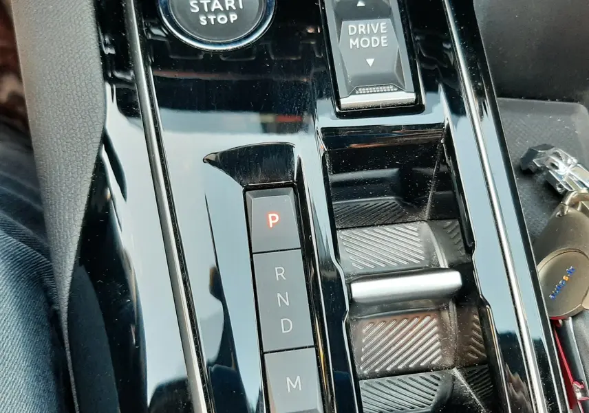 Gros plan sur la console centrale noire brillante du Peugeot 3008 gris, montrant les boutons de boîte auto et mode de conduite.