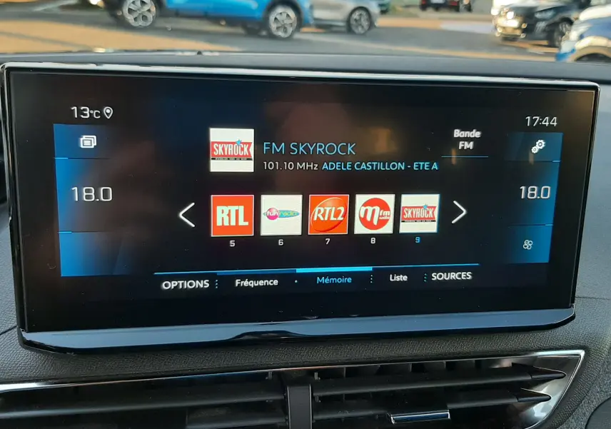 Écran central tactile du Peugeot 3008 gris platinium affichant les stations radio FM, avec la température intérieure à 18°C.