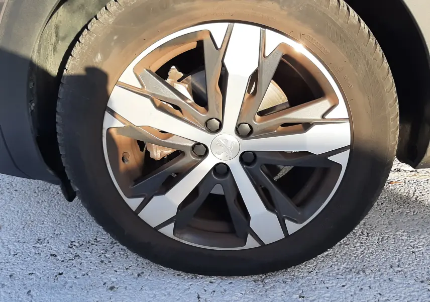 Gros plan sur la roue avant gauche du Peugeot 3008 gris platinium, mettant en valeur la jante alliage bicolore au design moderne.