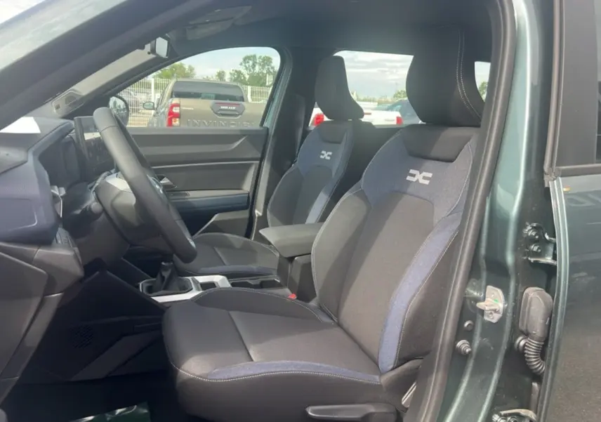 Vue intérieure côté conducteur du Dacia Bigster 2025 vert cèdre, mettant en valeur les sièges tissu avec logo DC brodé.