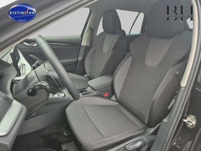 Intérieur avant de la Skoda Octavia Combi 2024, sièges tissu noir/gris et accoudoir central visible côté conducteur.