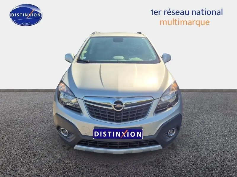 Vue frontale d'un Opel Mokka gris Astéroïde 2016 avec calandre chromée et phares halogènes allumés.