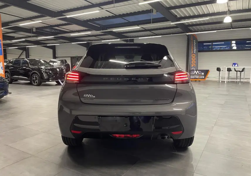 Vue arrière d'une Peugeot 208 hybride gris selenium avec feux arrière LED 3 griffes et bandeau noir brillant en intérieur showroom.