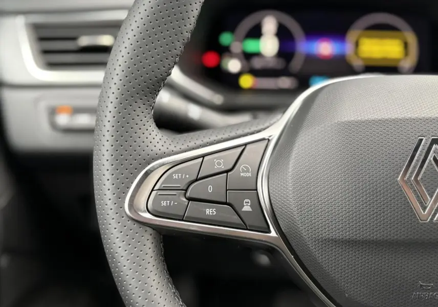 Gros plan sur le volant perforé noir du Renault Captur 2025 avec commandes intégrées et tableau de bord numérique flou.