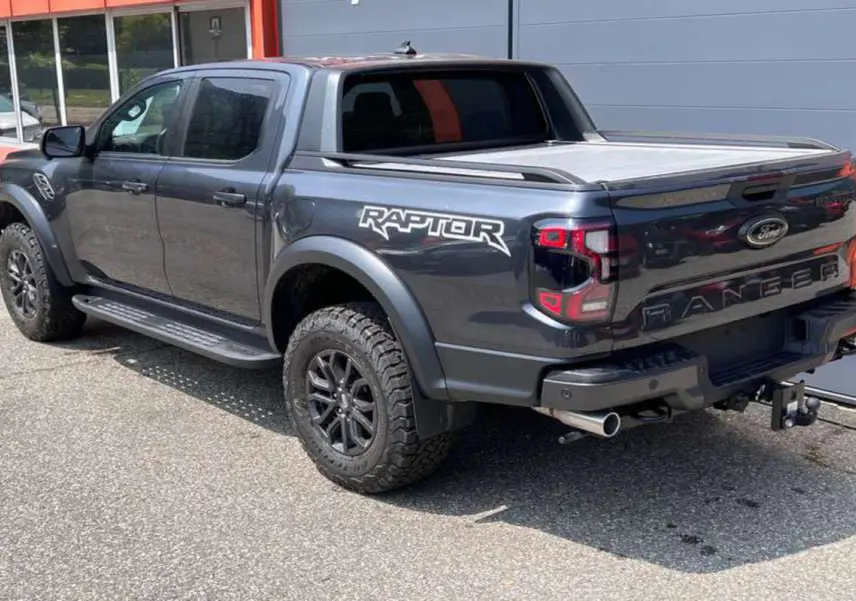 Vue 3/4 arrière droite du Ford Ranger Raptor gris météore avec logo Raptor et roues tout-terrain.