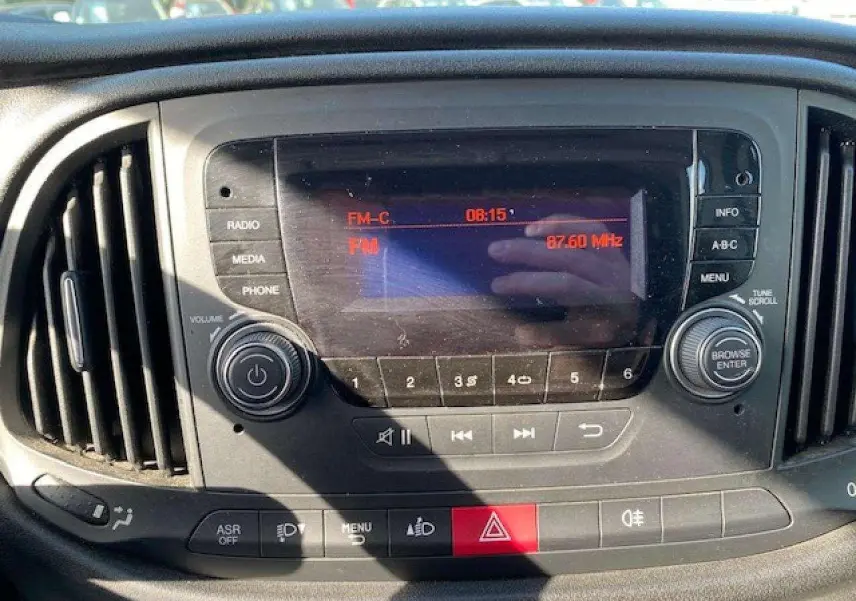 Vue rapprochée du tableau de bord du Fiat Doblo blanc 2017, mettant en valeur l’autoradio et les commandes centrales.