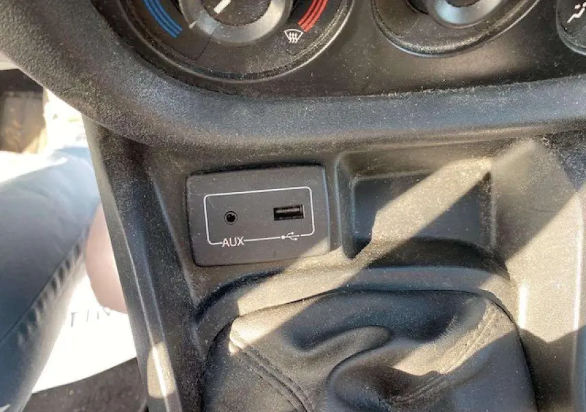 Vue rapprochée de la console centrale du Fiat Doblo blanc, montrant la prise AUX, port USB et commande de climatisation.