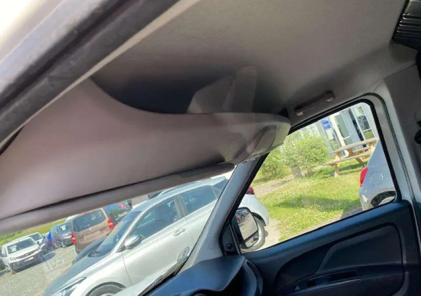 Vue intérieure côté conducteur du Fiat Doblo blanc, montrant le pare-soleil et la portière avec vitre.