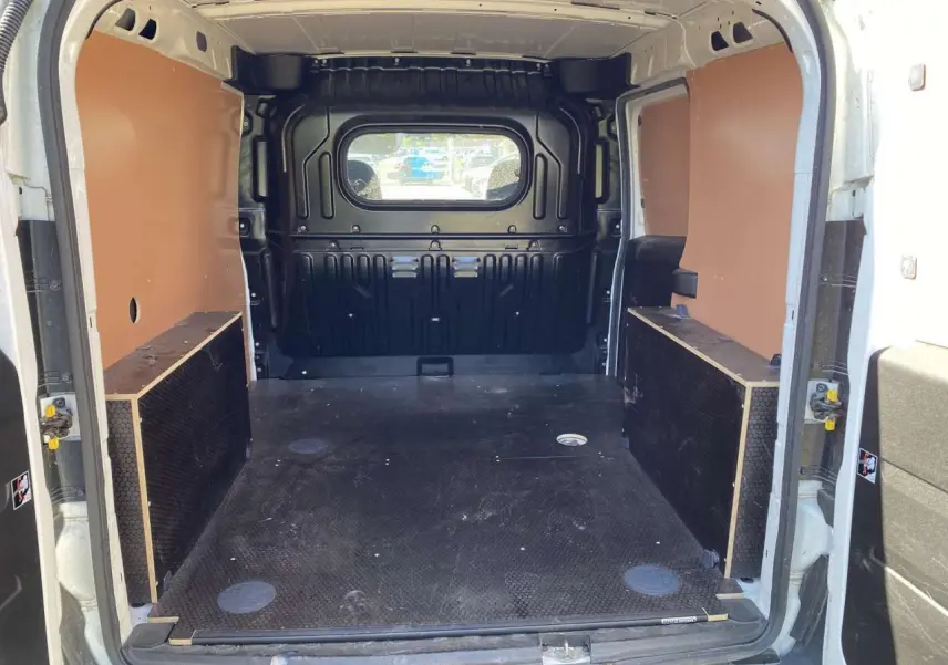 Vue intérieure arrière du fourgon blanc FIAT Doblo 2017 avec espace de chargement équipé d'un kit bois et paroi vitrée.