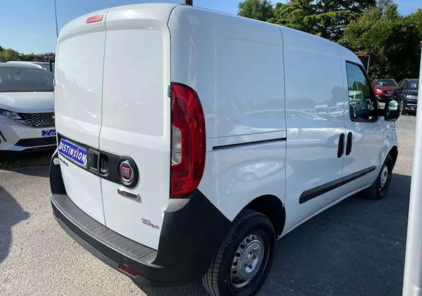 Fiat Doblo blanc vu en 3/4 arrière droit, fourgon tôlé avec pare-chocs noirs et porte latérale droite.