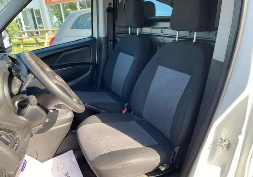 Vue intérieure côté conducteur du Fiat Doblo blanc 2017, montrant les sièges avant et la paroi de séparation vitrée.