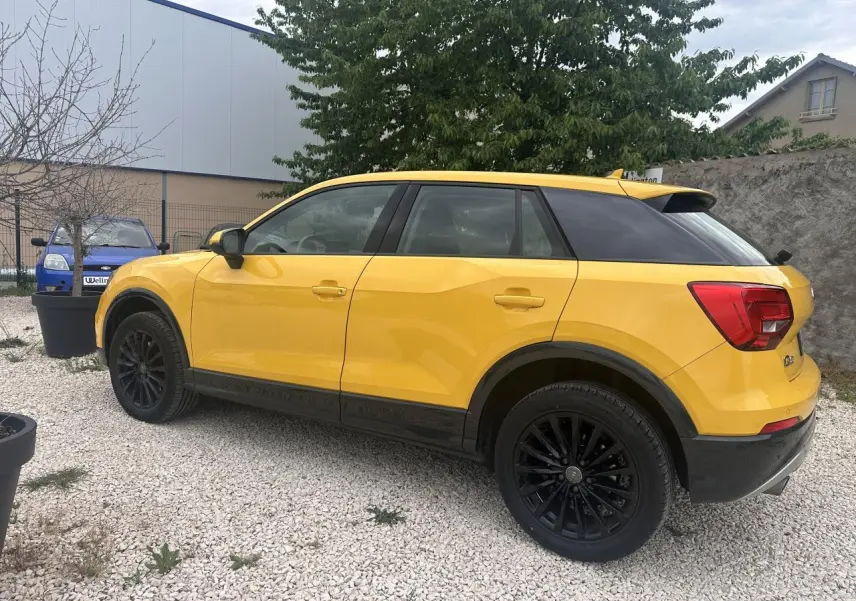 Audi Q2 jaune vue de profil côté gauche, avec jantes noires et toit noir contrastant visible en extérieur sur gravier.
