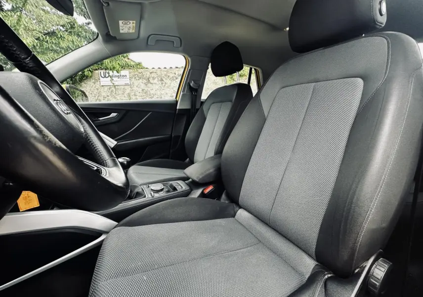 Vue intérieure côté conducteur de l'Audi Q2 1.6 TDI Business line 2017, sellerie tissu noir et gris, accoudoir central visible.