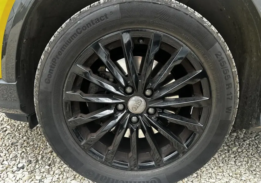 Gros plan sur la jante en aluminium noire multi-branches de l'Audi Q2 jaune, avec pneu Continental 215/55 R17 visible.