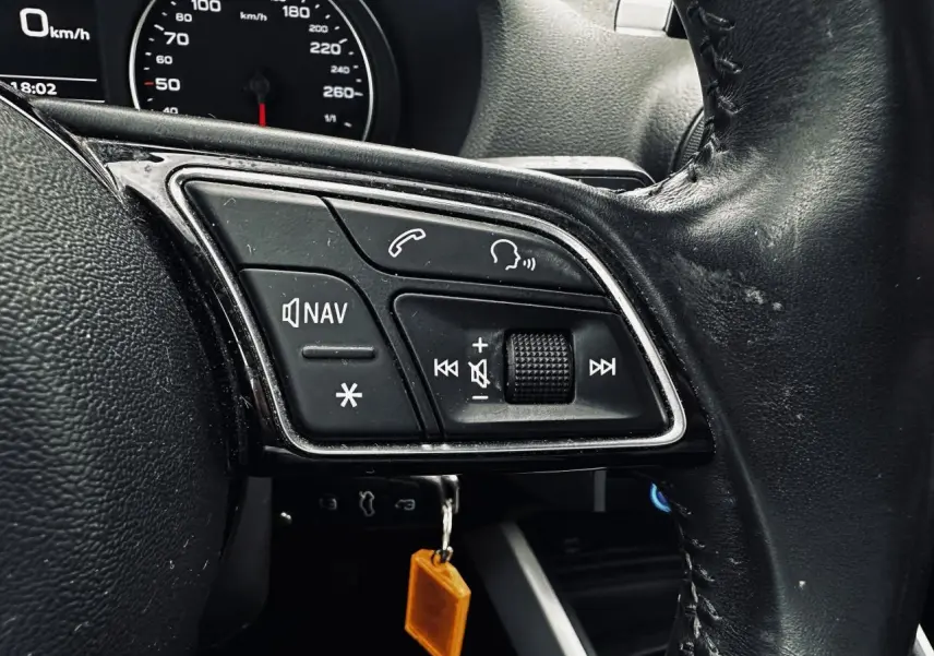 Gros plan sur les commandes gauche du volant en cuir noir de l'Audi Q2 1.6 TDI Business line, avec tableau de bord partiel visible.