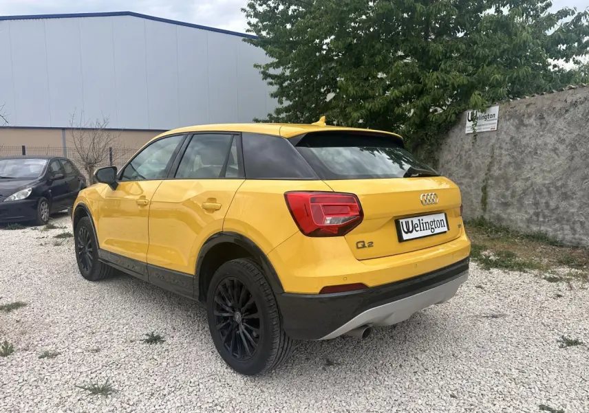 Audi Q2 jaune vue 3/4 arrière droit, avec jantes noires et détails noirs sur pare-chocs et bas de caisse.