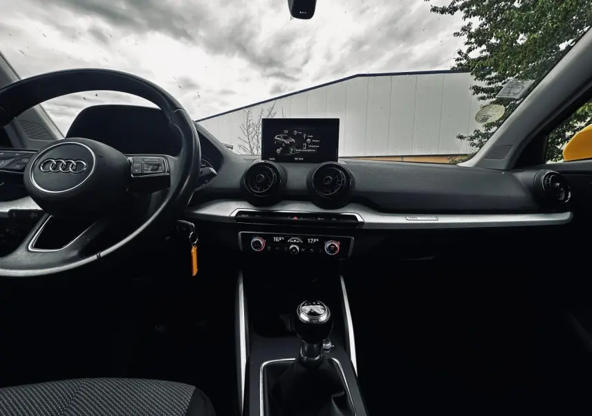 Vue intérieure avant de l'Audi Q2 jaune 2017, mettant en valeur le volant cuir, la boîte manuelle et l'écran central.