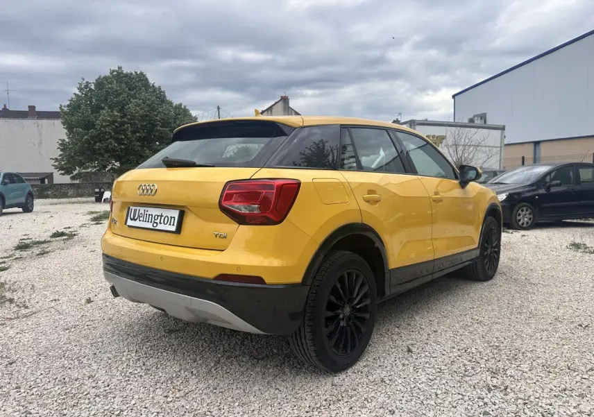 Audi Q2 jaune vue 3/4 arrière droit, jantes noires et toit noir contrastant sur un sol gravillonné.