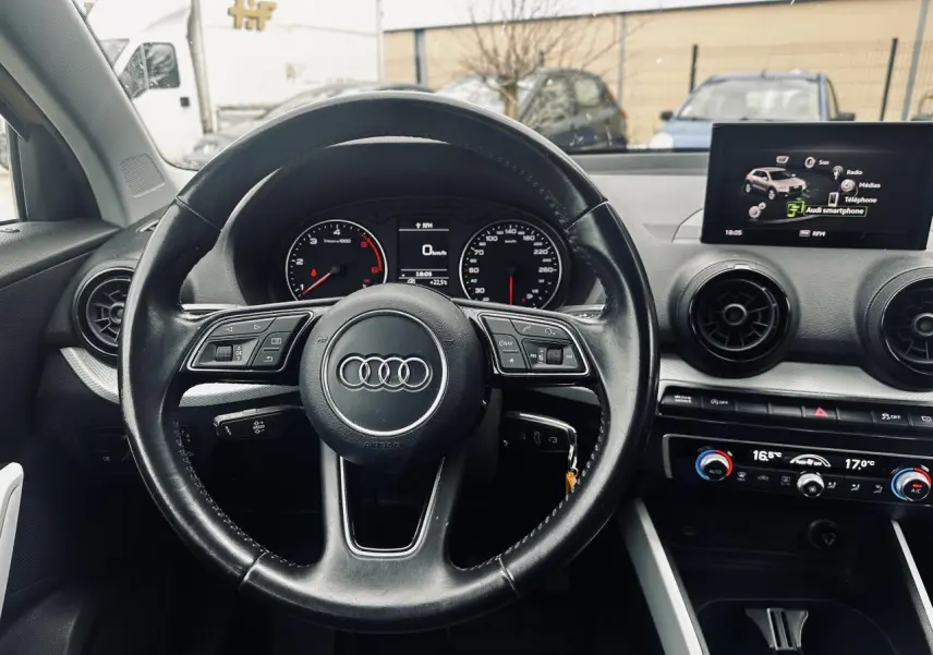 Vue intérieure centrée sur le volant multifonction noir de l'Audi Q2 1.6 TDI 2017 avec tableau de bord et écran multimédia.