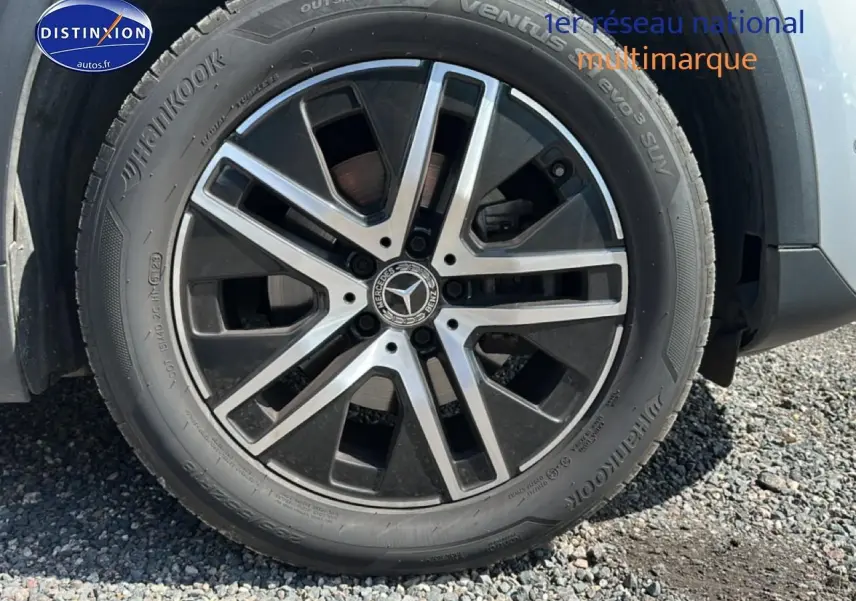 Gros plan sur la jante alu noire et argentée d’un Mercedes GLA gris, avec pneu Hankook visible sur gravier.