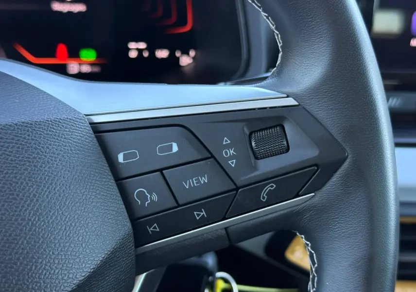 Gros plan sur les commandes multifonctions en cuir du volant côté gauche du SEAT Arona 2025 blanc et noir.