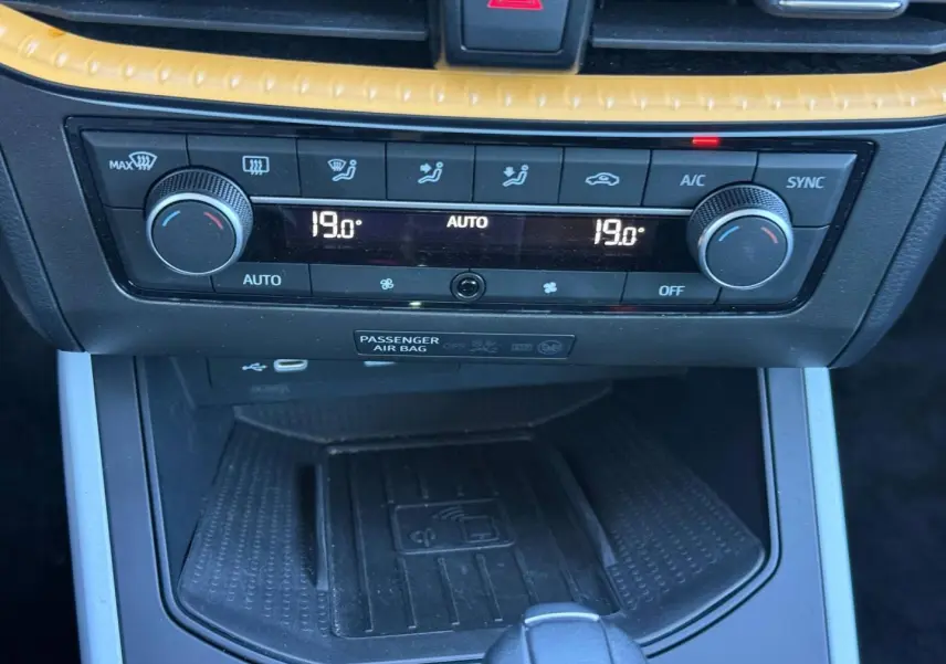 Vue rapprochée de la console centrale du SEAT Arona 2025, montrant la climatisation automatique et un chargeur sans fil noir.