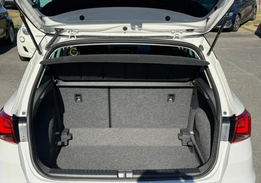 Coffre ouvert vu de l’arrière d’un SEAT Arona blanc Candy avec cache-bagages noir et intérieur gris.
