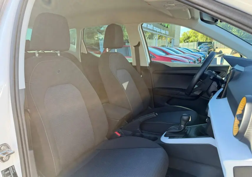 Vue intérieure côté gauche du SEAT Arona 2025, sièges tissu gris et console centrale avec levier de boîte auto.