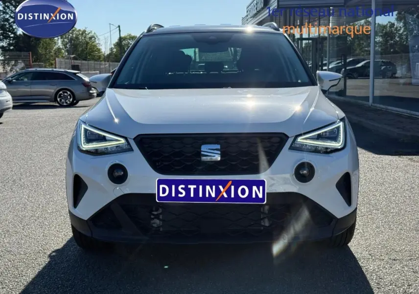 Vue frontale d'un SEAT Arona blanc Candy avec toit noir, feux LED allumés et calandre noire distinctive.