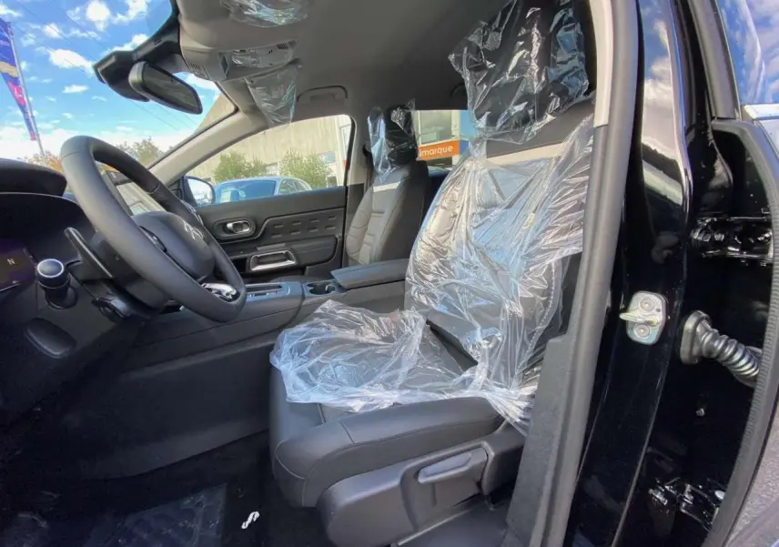 Intérieur avant du Citroën C5 Aircross noir Perla, sièges protégés par film plastique, volant et tableau de bord visibles.